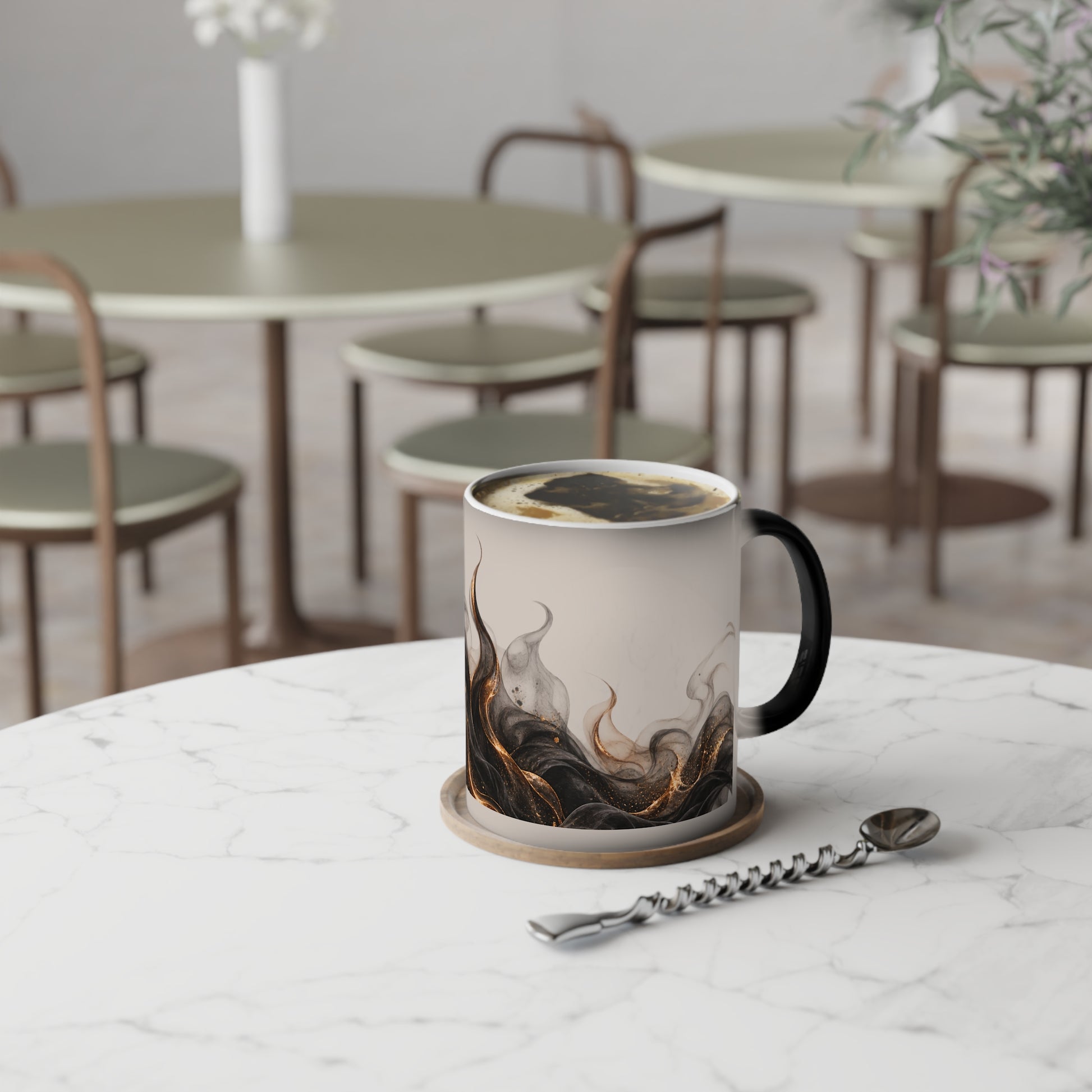A ceramic coffee mug with a black handle and a marbled smoke design in black, brown, and gold on a cream background, sitting on a marble table in a cafe setting.